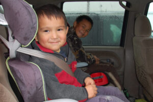 A smiling child buckled into a booster seat in a vehicle